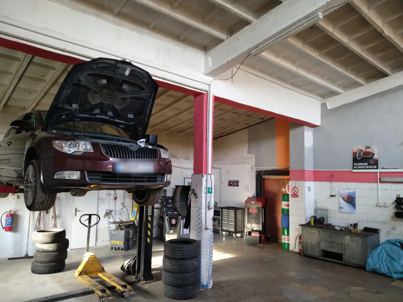 Dielňa Pneuservis-Autoservis PK: auto na zdviháku s otvorenou kapotou, vedľa pneumatiky a vyvažovačka